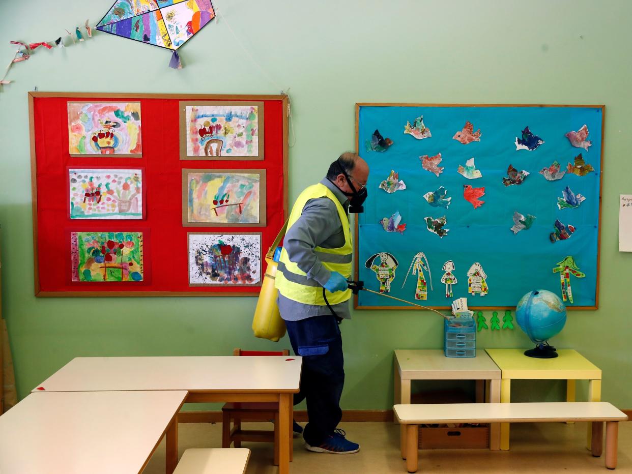 A worker wearing a protective mask sprays disinfectant inside a classroom of a kindergarten in the suburb of Halandri, northern Athens, Friday, May 29, 2020. Greece will reopen preschools, kindergartens and primary schools on Monday in the latest round of easing coronavirus pandemic restrictions imposed in late March. Classes will have no more than 15 children while the academic year will end on Friday, June 26. (AP Photo/Thanassis Stavrakis)