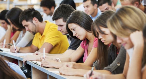 'Group of college students in the university amphitheatre, they are sitting and doing an exam. The focus is on the brunette in p