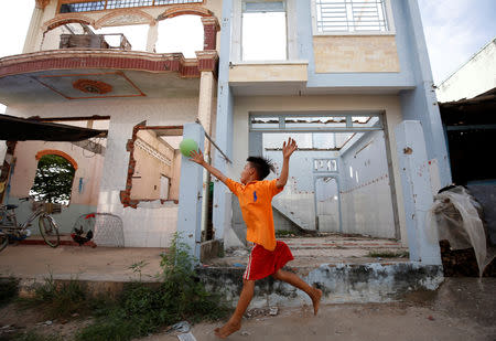 A boy plays with a ball in front of collapsed houses damaged by landslide along Mekong river in An Giang province, Vietnam December 17, 2018. Picture taken December 17, 2018. REUTERS/Kham