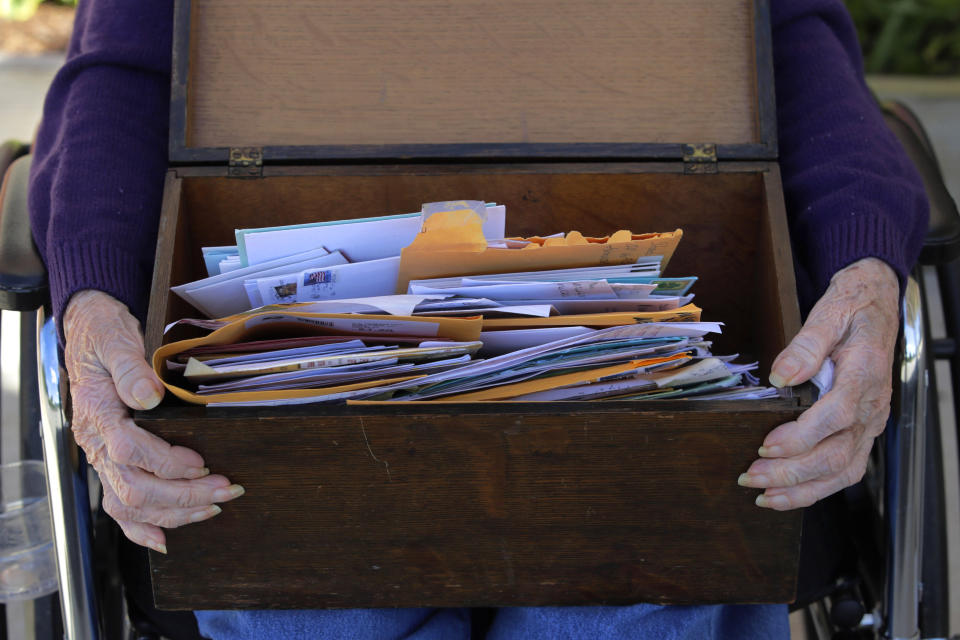 In this Monday, June 8, 2020, photo, 93-year-old Flo Young, originally from Cambridge, Mass., rests a box of pen pal letters on her lap outside the Sullivan County Health Care nursing home in Unity, N.H In a letter-writing effort during the virus pandemic to connect nursing home residents in two neighboring communities, residents now are receiving pen pal letters from across the United States. (AP Photo/Charles Krupa)