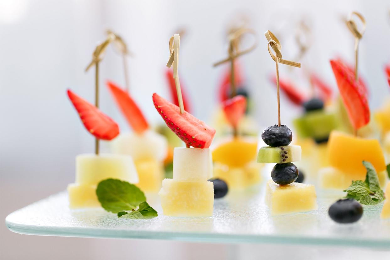 Focus on several fruit skewers on a glass serving tray with a blurred background of whites and grays