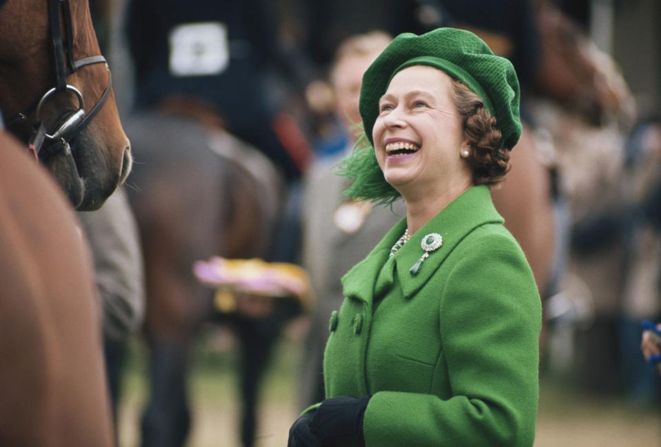 Circa 1980: Queen Elizabeth II, wearing a green coat and matching hat, laughing as she attends the Royal Windsor Horse Show, held at Home Park in Windsor, Berkshire, England, Great Britain, circa 1980.