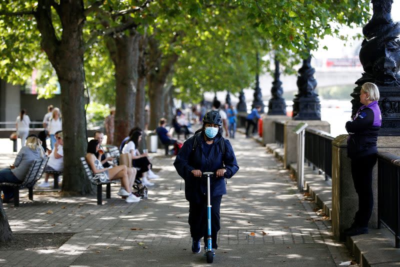 FILE PHOTO: A woman wearing a protective face mask rides a scooter along the South Bank, amid the spread of coronavirus disease (COVID-19), in London