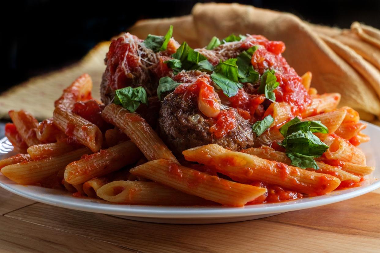 Italian penne rigate pasta with sugo all'arrabbiata sauce and meatballs garnished with chopped basil and parmesan cheese