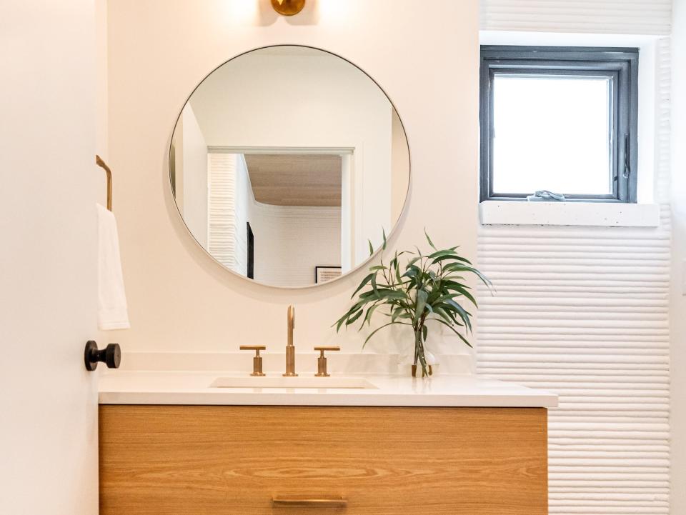 a bathroom vanity with a sink, round mirror, lights, and a window