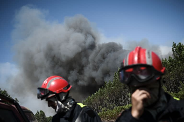 Los bomberos se encuentran en una carretera mientras se ve un fuerte humo en el fondo durante los incendios forestales cerca de la ciudad de Origne, suroeste de Francia, el 17 de julio de 2022.