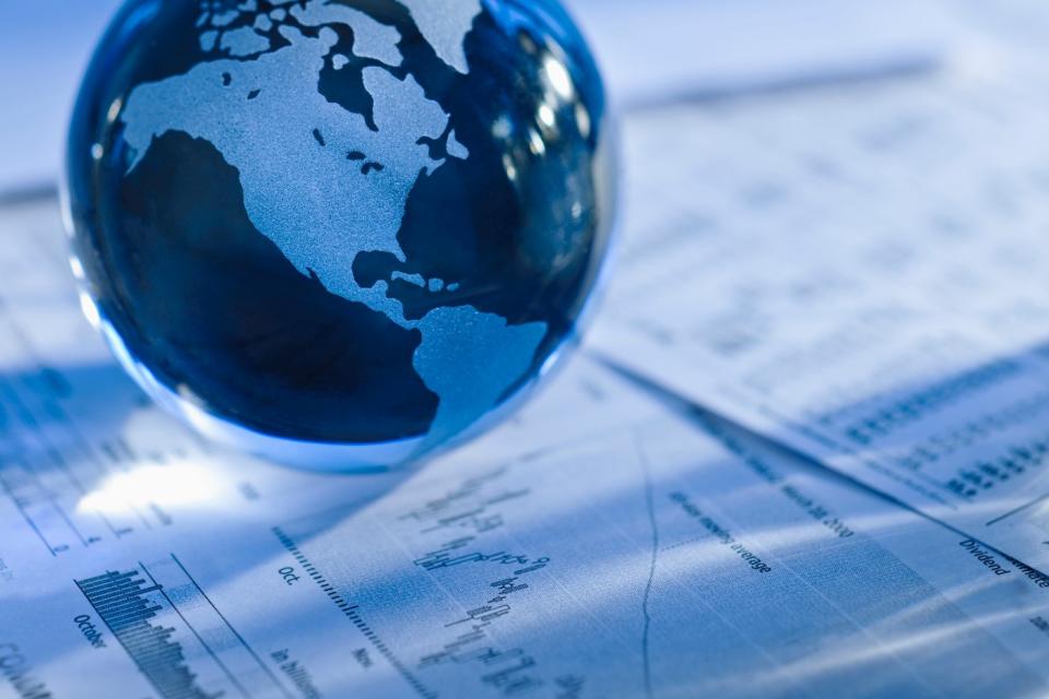 A small glass globe mounted on top of a document showing financial information and stock charts. 