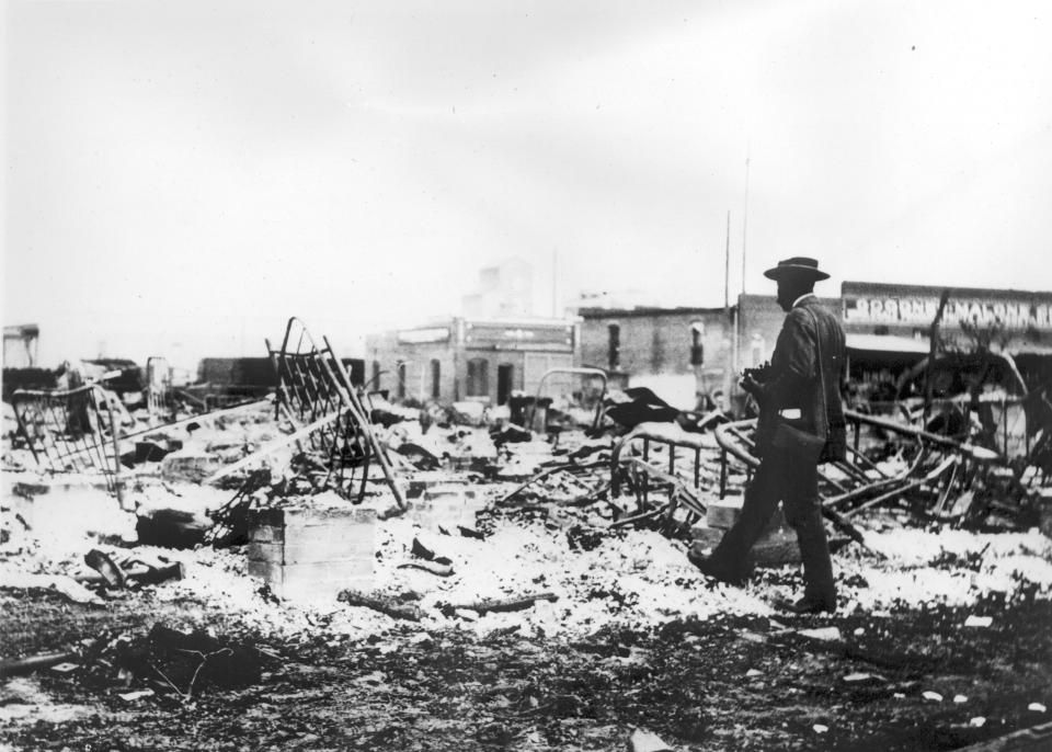 An African-American man with a camera looking at the skeletons of iron beds which rise above the ashes of a burned-out block after the Tulsa Race Massacre, Tulsa, Oklahoma, June 1921. (Photo by Oklahoma Historical Society/Getty Images)