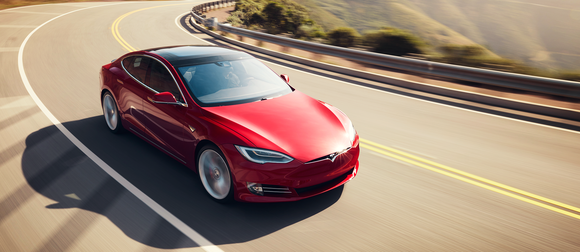 A red Tesla Model S on a scenic road.