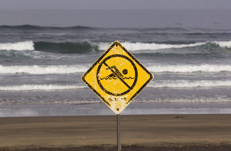 A no swimming sign is displayed at Muriwai Beach near Auckland, New Zealand, Thursday, Feb. 28, 2013, a day after Adam Strange was killed by a shark. About 150 friends and family of Strange, 46, wrote messages to him in the sand and stepped into the water Thursday at a New Zealand beach to say goodbye after he was killed Wednesday by a large shark. (AP Photo/New Zealand Herald, Brett Phibbs) New Zealand Out, Australia Out