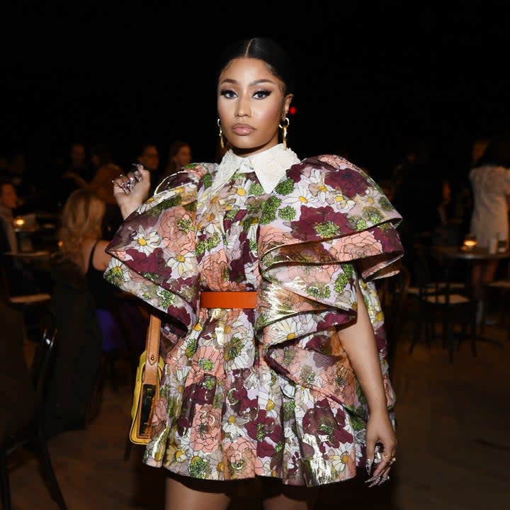 Full-body shot of Nicki Minaj wearing a floral, ruffle dress and tan suede boots