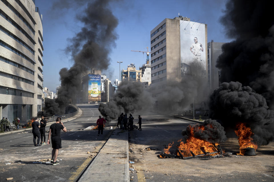 Protesters stand next to burning tires set on fire to block a main road, after the Lebanese pound hit a record low against the dollar on the black market, in Beirut, Lebanon, Saturday, March 6, 2021. (AP Photo/Hassan Ammar)