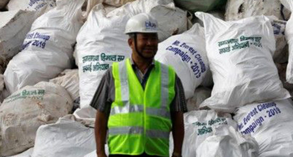 A man stands in front of the piles of garbage collected, in bags labelled "Mt Everest Cleanup 2019". 