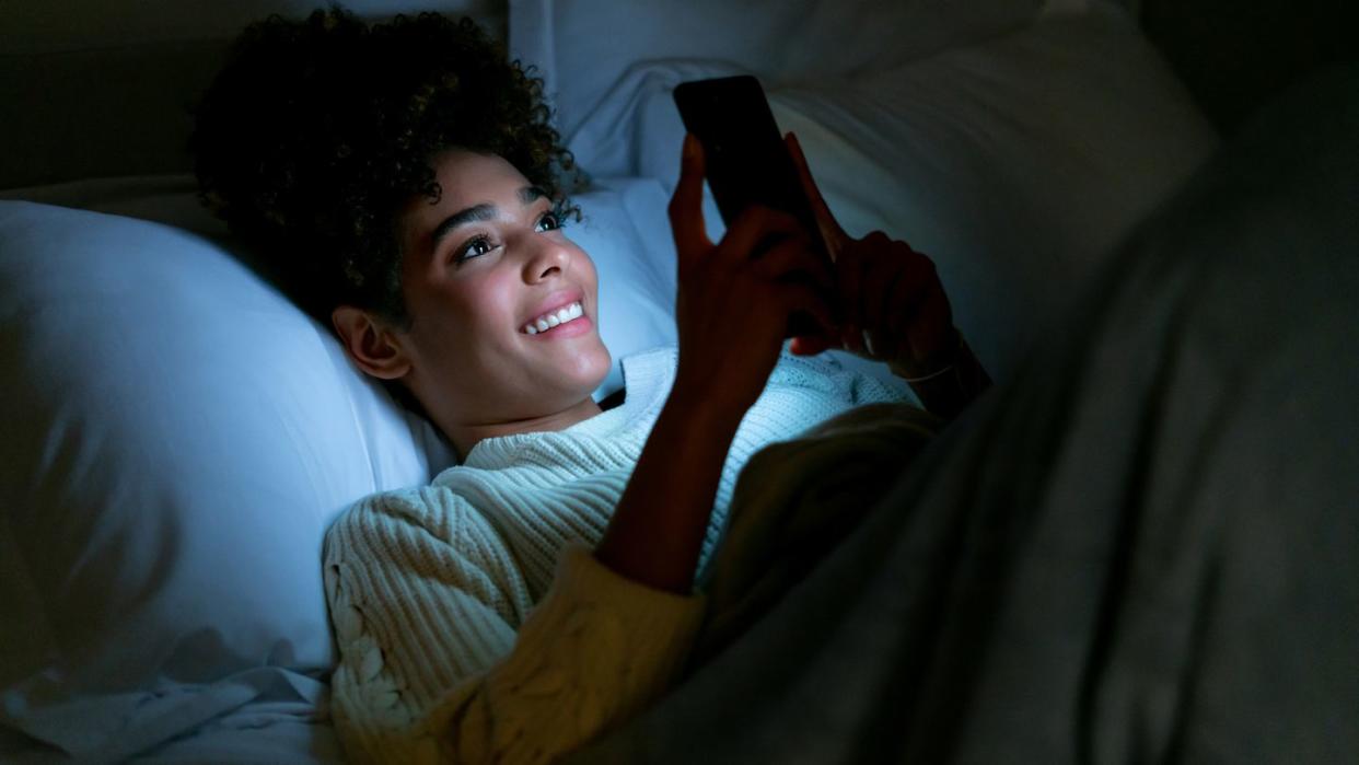 happy woman in bed texting on her cell phone
