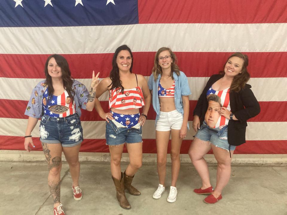 Sierra Estep, Elyse Parrish, Leslie Taylor and Asia Henderson wear outfits with the faces of their 82nd Airborne Divison paratrooper husbands Tuesday, June 28, 2022, at Fort Bragg's Green Ramp, as they wait for their husbands to return home from a deployment to Poland.