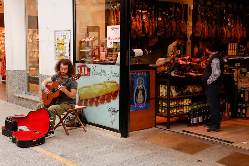 A street musician plays a guitar as a worker cuts ham in a shop in Ronda