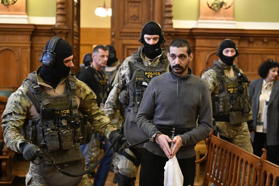 A Syrian man identified as Hassan F., centre, is escorted by Police officers as he arrives at the Metropolitan Court in Budapest, Hungary, Wednesday, Nov. 13, 2019. Prosecutors said the 27-year-old man identified only as Hassan F. participated in the beheading of a religious leader in the city of al-Sukhnah in Homs province and was also involved in the killings of at least 25 people. (Zsolt Szigetvary/MTI via AP)