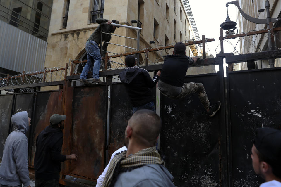 Anti-government protesters climb a metal wall installed by security forces to prevent protesters from reaching the Parliament building, during a protest in Beirut, Lebanon, Saturday, March. 13, 2021. Riot police fired tear gas to disperse scores of people who protested near parliament building in central Beirut Saturday amid deteriorating economic and financial conditions and as the local currency hit new low levels. (AP Photo/Bilal Hussein)