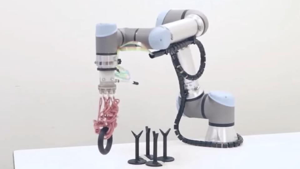A robotic arm with soft pink tentacles that curl to pick up a black ring