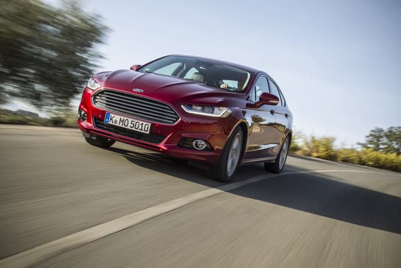 A red Ford Mondeo, a midsize sedan, with a European license plate. It looks nearly identical to a Ford Fusion.