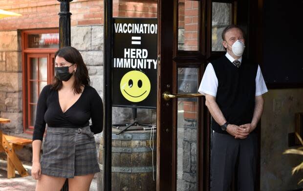 A sign encouraging vaccination is seen at the doors of Ottawa's Lieutenant's Pump pub as staff watch patrons arrive on June 11, the first day it could serve again on its patio under Ontario's latest reopening plan. (Justin Tang/The Canadian Press - image credit)