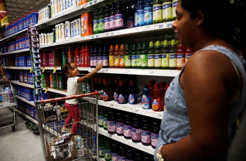 FILE PHOTO: Child stands on a shopping cart as she points cleaning products next to her mother at a supermarket in Sao Paulo