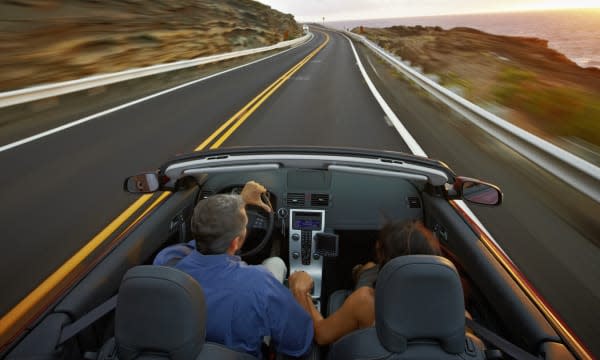 Husband and wife driving convertible at sunrise