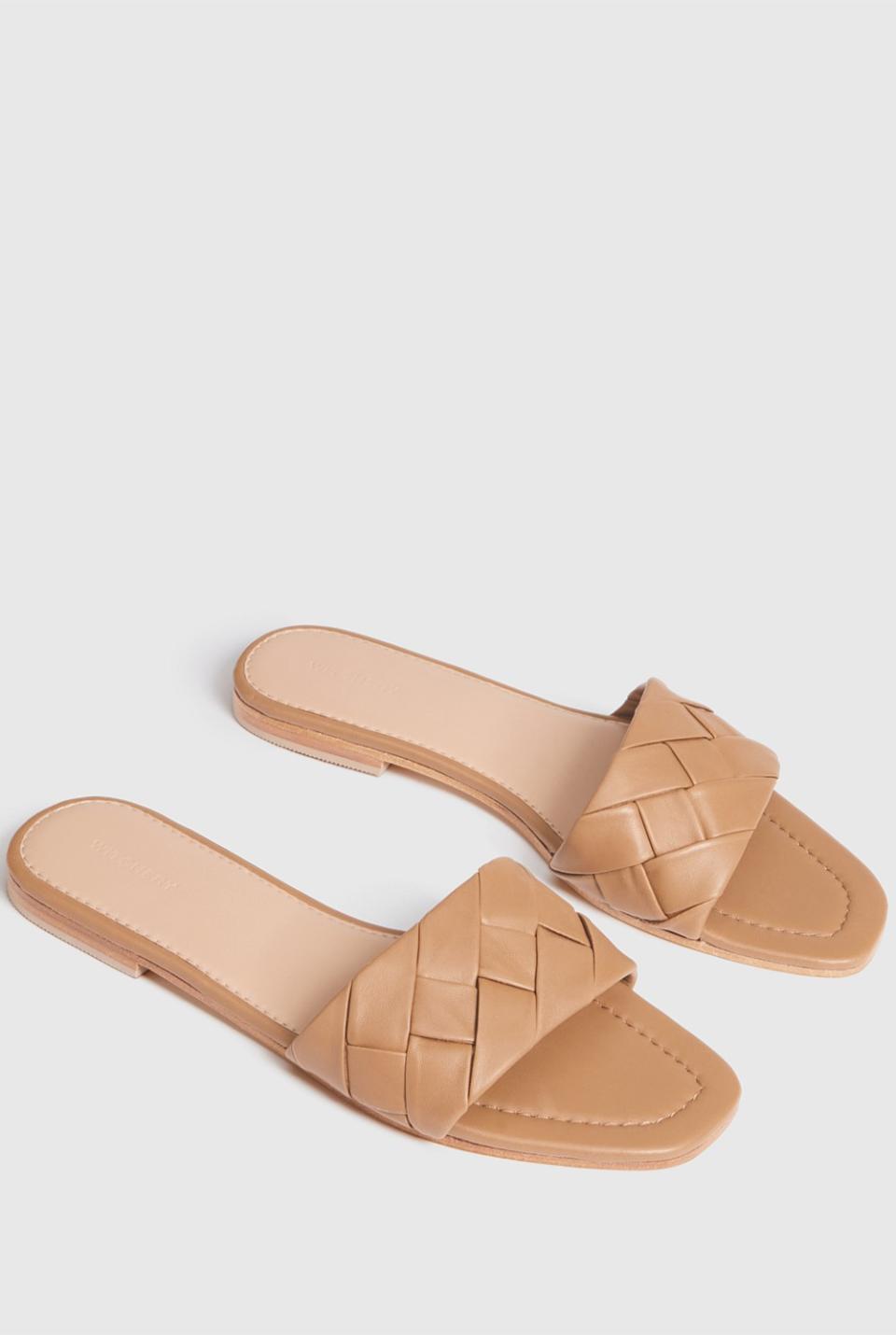 A pair of beige Nala Leather Slides, $49.95, from Witchery, with woven straps and paler lining sit on a pale surface.