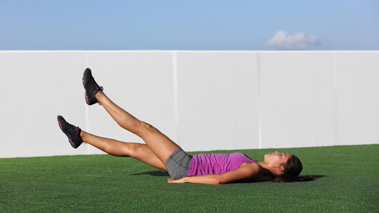  Woman doing scissor kicks on grass outside. 