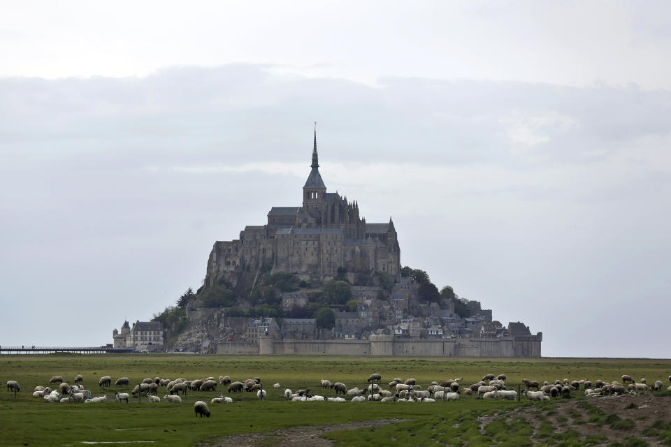 FILE - Sheeps graze in the fields around the Mont Saint Michel, Wednesday, May 8, 2018, in western France. France’s beloved abbey of Mont-Saint-Michel has reached a ripe old age. It's been 1,000 years since the laying of its first stone. The millennial of the UNESCO World Heritage site and key Normandy tourism magnet is being celebrated until November with exhibits, dance shows and concerts. French President Emmanuel Macron is heading there on Monday, June 5, 2023. (AP Photo/Thibault Camus, File)