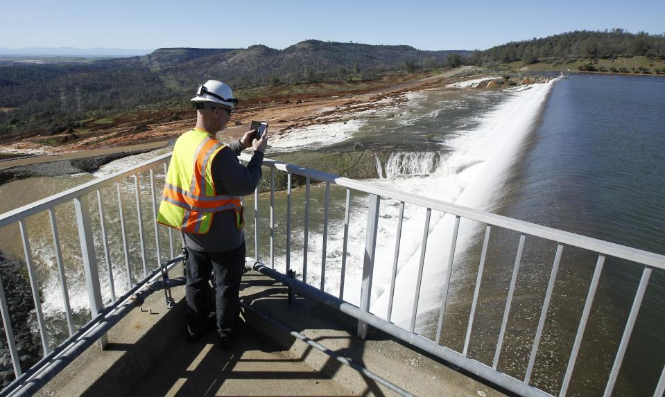 Jason Newton, of the Department of Water Resources, takes a picture of water going over the emergency spillway at Oroville Dam Saturday, Feb. 11, 2017, in Oroville, Calif. Water started flowing over the emergency spillway at the nation's tallest dam for the first time Saturday after erosion damaged the Northern California dam's main spillway. (AP Photo/Rich Pedroncelli)