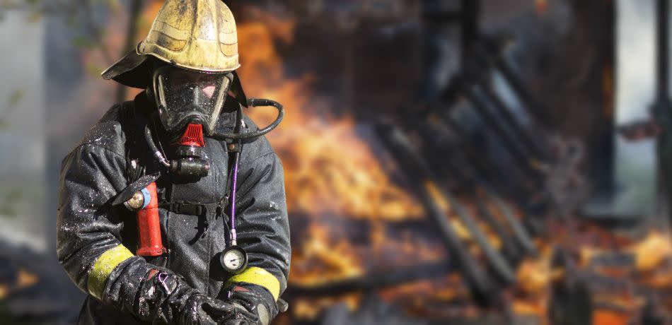 Fire fighter with protective gear stands outside a house blaze