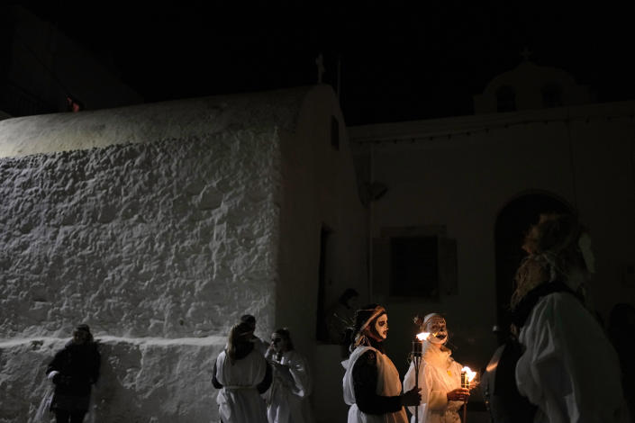 Young men and women with faces painted wear white sheets and hold torches on long poles, take part at the Torch Parade (Lampadiforia) on the Aegean Sea island of Naxos, Greece, late Saturday, Feb. 25, 2023. The first proper celebration of the Carnival after four years of COVID restrictions, has attracted throngs of revellers, Greek and foreign, with the young especially showing up in large numbers. (AP Photo/Thanassis Stavrakis)