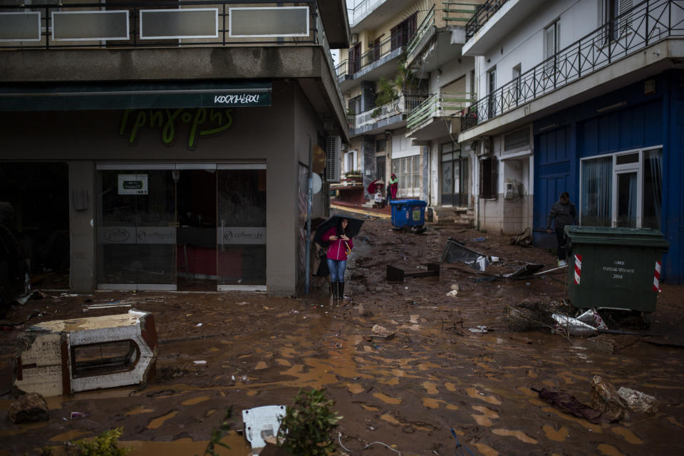 A woman with an umbrella stands in a flooded street next to a damaged shop. (Photo: Angelos Tzortzinis/AFP/Getty Images)