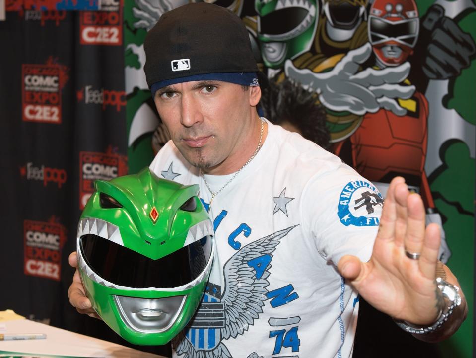 Jason David Frank with a backward cap holding Green Power Ranger helmet