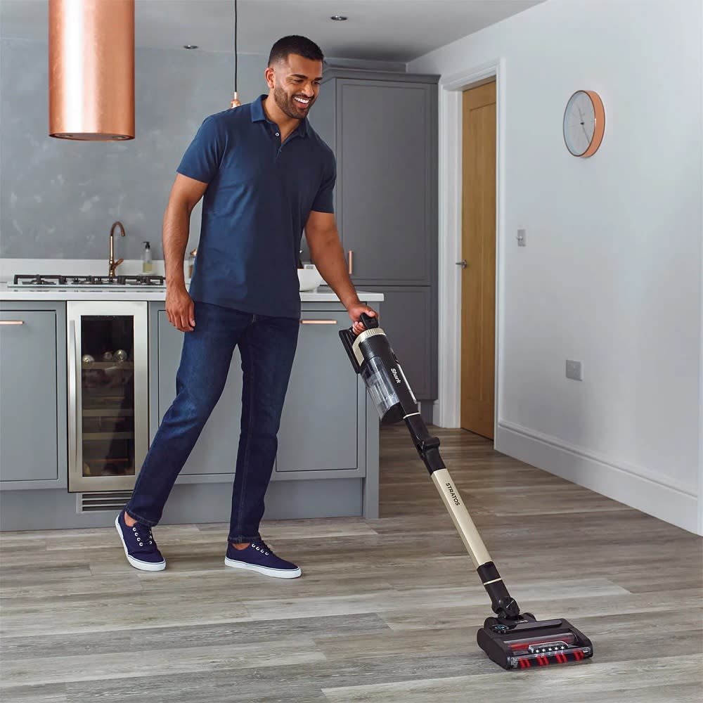 A person using a Shark cordless vacuum on a wooden floor. 