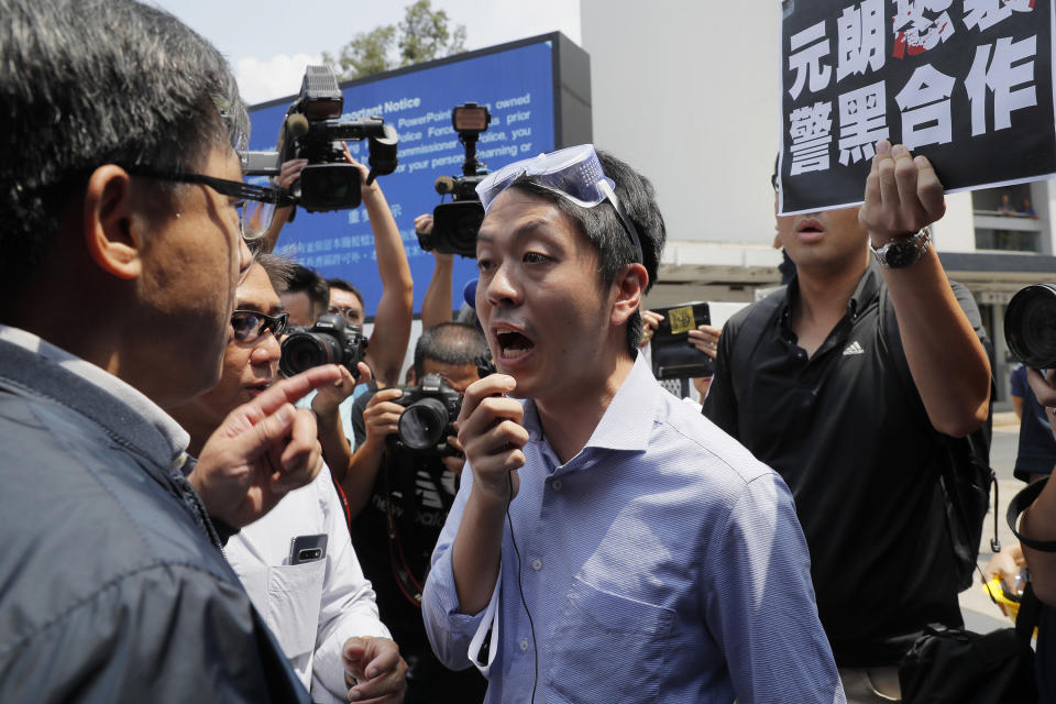 Pro-democracy lawmakers Lam Cheuk-ting, right in black shirt, and Ted Hui, center, argue with pro-Beijing lawmaker Junius Ho, left, during a demonstration of an anti-riot vehicle equipped with water cannon at the Police Tactical Unit Headquarters in Hong Kong on Aug. 12, 2019. Hong Kong police on Wednesday morning, Aug. 26, 2020 arrested 16 people on charges related to anti-government protests last year, including two opposition lawmakers Hui and Lam. The placard reads "Yuen Long terrorist attack, collusion between police and triads." (AP Photo/Kin Cheung)