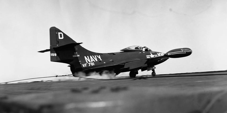 Close view of an F9F Panther jet touching down on the deck of the USS Oriskany, tail hook engaging the arresting wire, smoke coming from impact of tires. Nov. 1952.