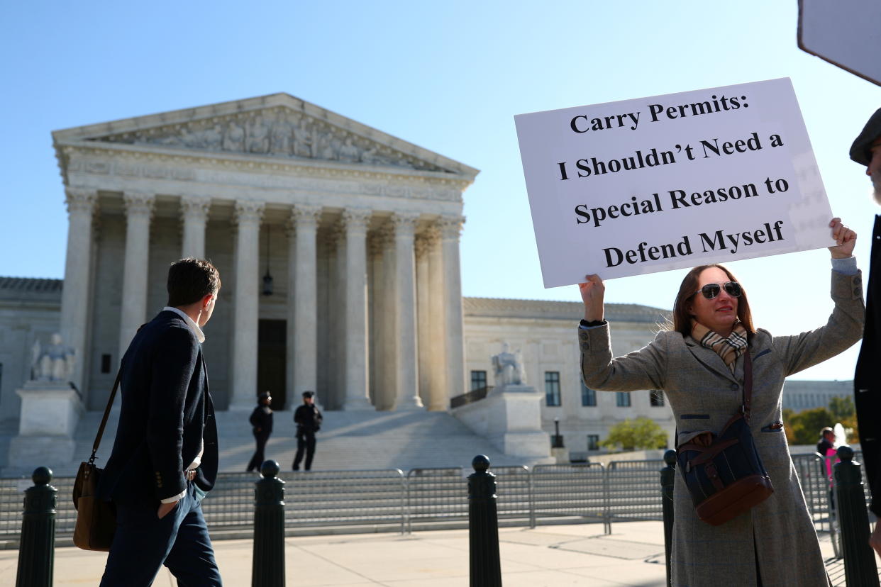 Katie Novotny, with the Supreme Court in the background, holds a sign saying: Carry Permits: I Shouldn't Need a Special Reason to Defence Myself.
