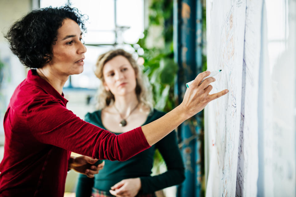 An office manager is writing on some whiteboard documents during a meeting with her colleagues.