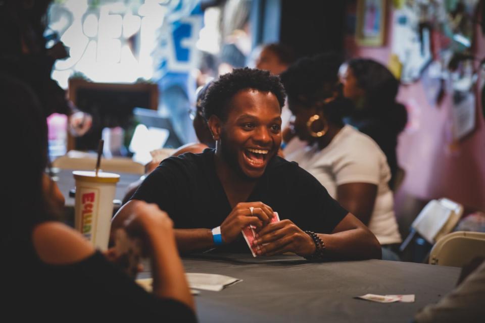 A man with a big smile on his face holds a hand of cards at a game table