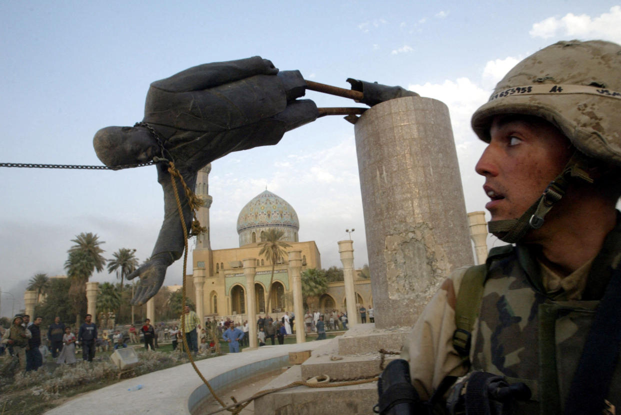 A U.S. soldier watches in surprise as a statue of Iraq's President Saddam Hussein, attached by a noose around the neck, falls at a right angle to its plinth.
