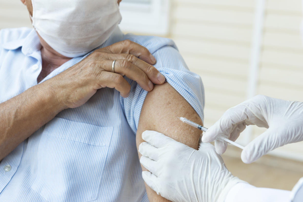 Senior man wearing a protective face mask is getting vaccination from a person with white surgical gloves.