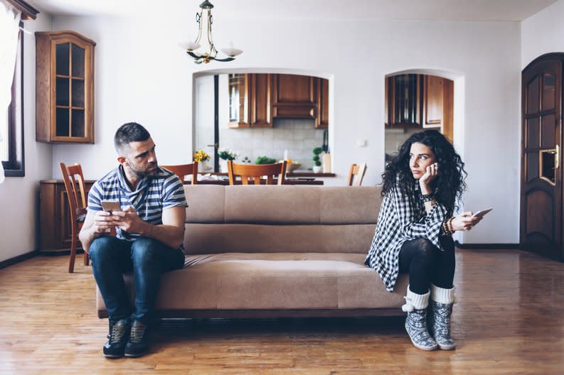 man and woman sitting at opposite ends of a couch and looking upset