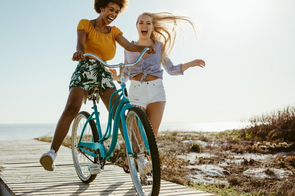 cheerful female friends having fun with a cycle outdoors two girls playing with a bicycle on the boardwalk on seaside