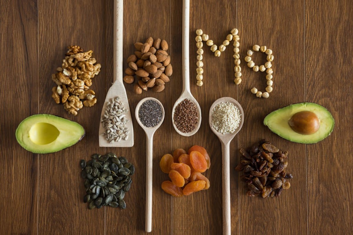 Wooden spoons with healthy seeds, nuts and dried fruits and word Mg arranged on wooden table<p>iStock</p>