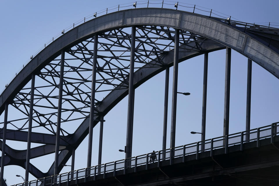 A pedestrian walks across the Centennial Bridge, Monday, Dec. 20, 2021, in Davenport, Iowa. The 81-year-old bridge across the Mississippi River creaks under the weight of tens of thousands of cars and trucks every day. Rust shows through its chipped silver paint, exposing the steel that needs replacing. This city's aging landmark is among more than 1,000 structurally deficient bridges in the area. The tally gives Iowa's 2nd congressional district the dubious distinction of having the second-most troubled bridges in the country. (AP Photo/Charlie Neibergall)