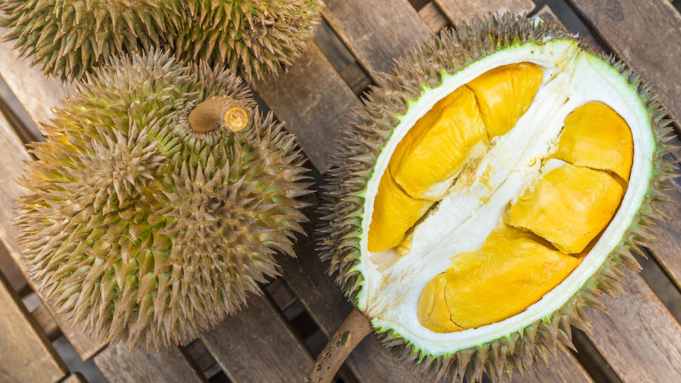 A picture of an unopened durian and an opened one in a wooden table.
