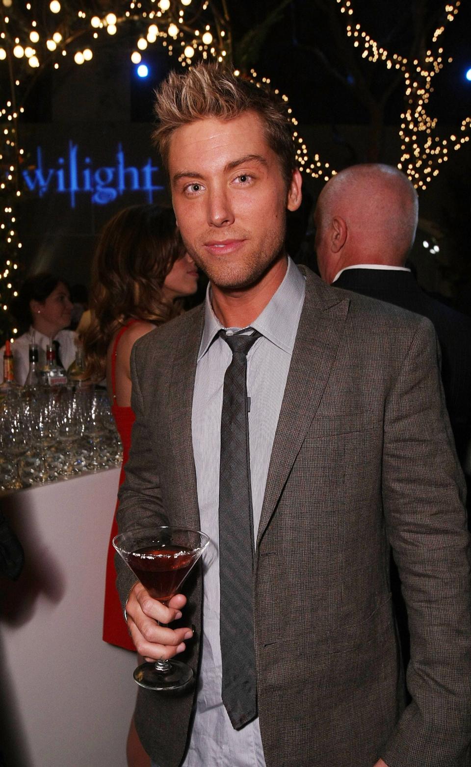 Lance Bass in a grey jacket holding a drink