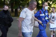 A Russian Emergency Situations Ministry paramedic, right, and a police officer escort a wounded man from a fire place at a warehouse in Moscow, Russia, Saturday, June 19, 2021. A large fire broke out at a fireworks depot in the center of Moscow. The fire is raging at the area of 500 square meters, Russia emergency services said in the statement. (AP Photo/Pavel Golovkin)